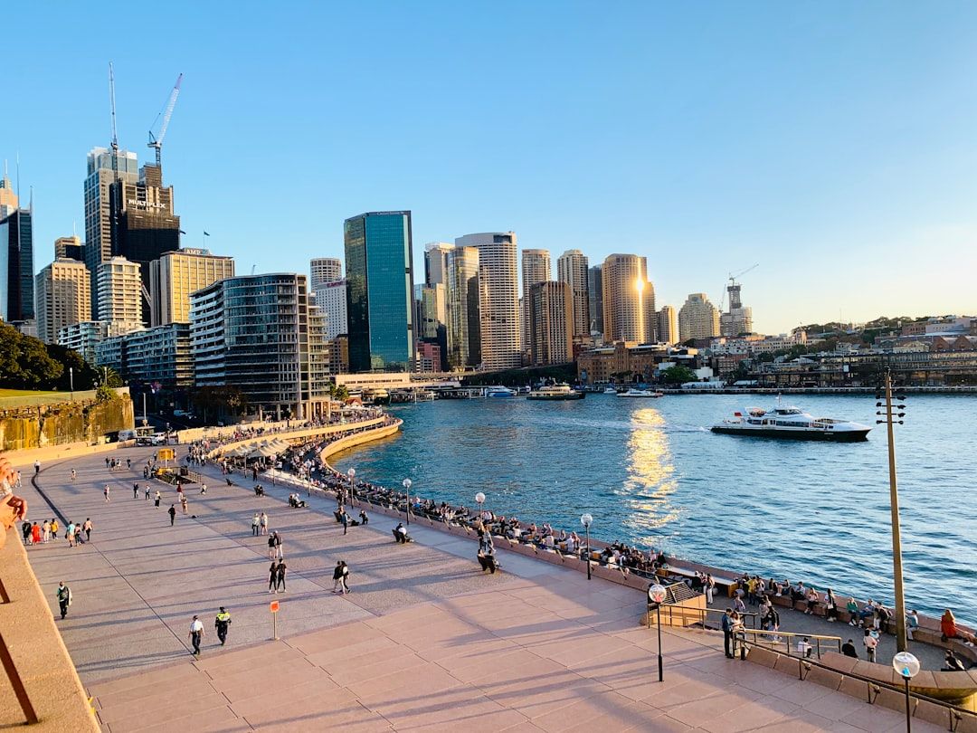 Modern car parked near Sydney Harbour Bridge and Opera House, with a rideshare car in the background, illustrating transport