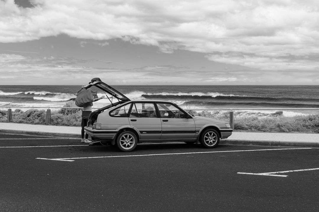 A person performing a thorough exterior inspection of a rental car, checking a tyre in a sunny Australian landscape.